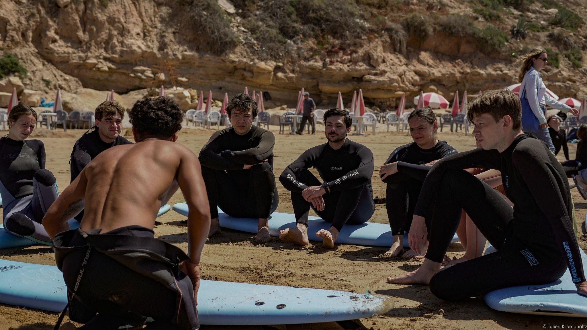 A group listening to Jamal during a beach briefing before their surf lesson